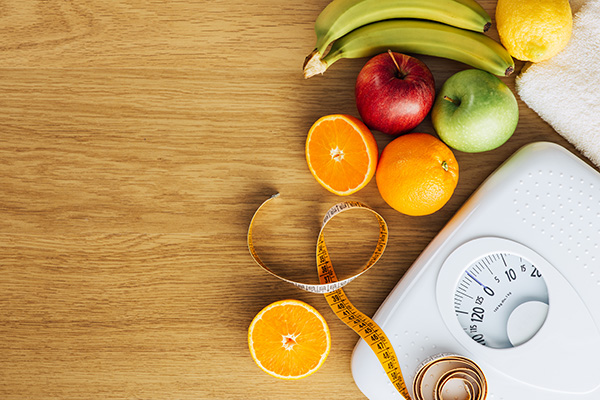 a body weight scale flanked by a measuring tape and a variety of fruit