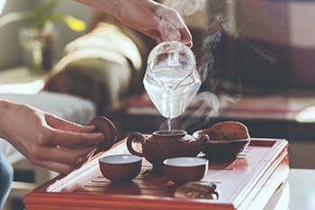 a person pours steaming hot water into an iron teapot to make green tea