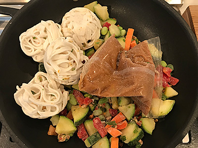 frozen vegetables, wads of frozen rice noodles, and a plastic bag containing what appears to be frozen sauce